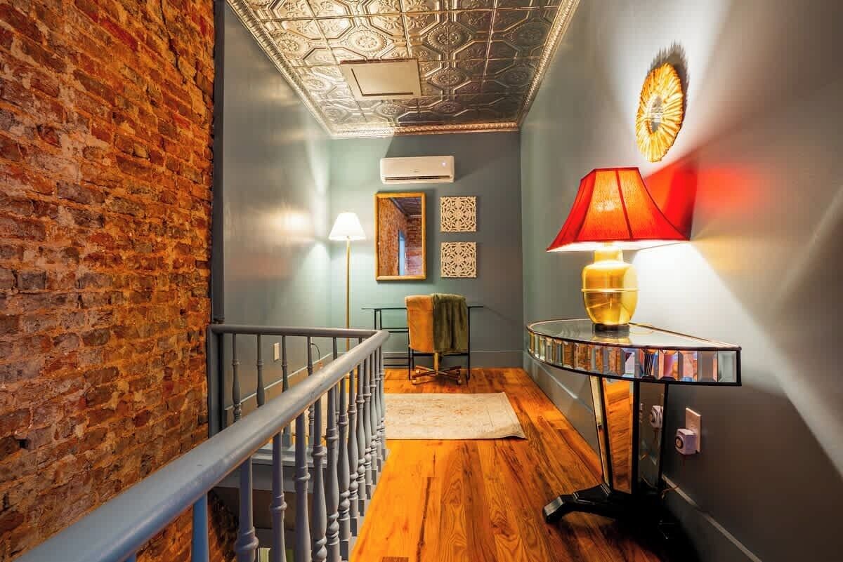 A staircase with a wooden floor and a brick wall, a ceiling with a geometric pattern, and a table with a red lamp.