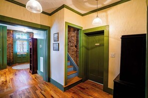A hallway with wooden flooring, green walls, a brick wall, and a staircase.