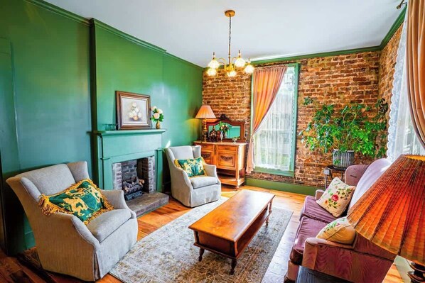 Un salon doté d’une cheminée, de murs verts, d’un mur d’accent en briques et d’une grande fenêtre avec des rideaux.