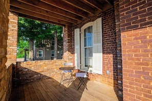 A covered porch with a brick wall, a window with shutters, and a small table with chairs.