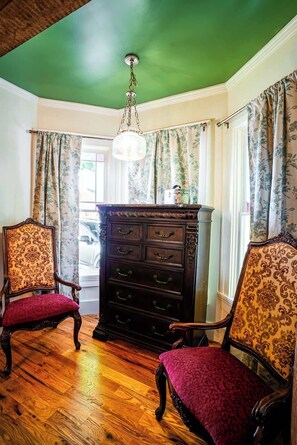 Une pièce avec deux fauteuils richement décorés, un buffet en bois sombre et un plafond vert.