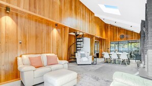 A modern interior with wooden panel walls, a white sofa, a dining area, and a staircase. - Private Pool, Tennis Court, Outdoor BBQ Cozy Lodge (Loch Sheldrake)