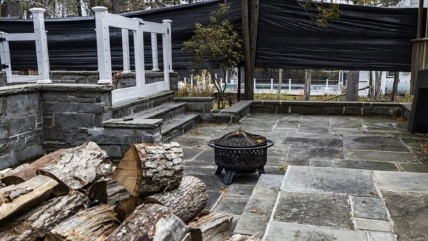 A stone patio with a fire pit and wood logs. - Private Pool, Tennis Court, Outdoor BBQ Cozy Lodge (Loch Sheldrake)