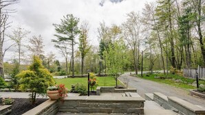 A paved patio with stone steps leading to a grassy area, surrounded by trees and a wooden fence. - Private Pool, Tennis Court, Outdoor BBQ Cozy Lodge (Loch Sheldrake)