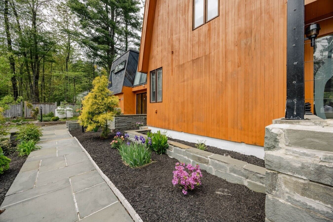 Ein modernes Haus mit Holzfassade, einem Kiesweg und einem Garten mit verschiedenen Pflanzen und Blumen.