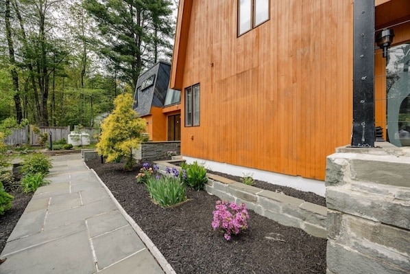 A modern house with a wooden exterior, a stone pathway, and a garden with various plants and flowers.