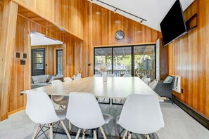 A conference room with a long table, white chairs, wooden panel walls, a clock, and a TV mounted on the wall.