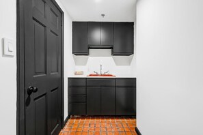 Uma cozinha compacta com armários escuros, bancada branca e pia vermelha.