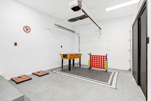 A room with a foosball table, a red and green pinball machine, and a projector mounted on the ceiling.