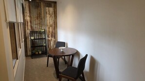 Un petit coin repas avec une table ronde et deux chaises, une étagère en métal pour les plantes et une porte en bois avec un rideau.