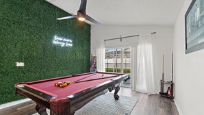Ein Billardtisch mit grüner Wand und Deckenventilator darüber.