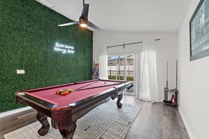 Ein Billardtisch mit grüner Wand und Deckenventilator darüber.