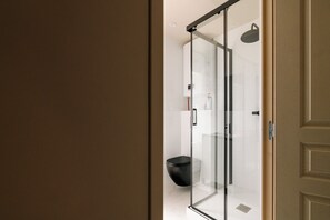 Une salle de bain moderne avec une douche à l’italienne en verre, des toilettes noires et un sol carrelé de couleur blanche.