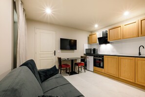 Ein gemütlicher Wohnbereich mit Sofa, Esstisch, einer Küche mit Holzschränken und einem an der Wand befestigten Fernseher.