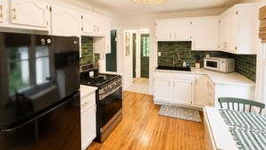 A modern kitchen with white cabinetry, a black refrigerator, a stove, and a microwave. - Couples King Bed Cottage with Fire Pit & Swing, Near Asheville & Biltmore in WNC (Leicester)