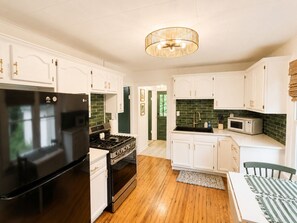 A modern kitchen with white cabinetry, a black refrigerator, a stove, and a microwave.