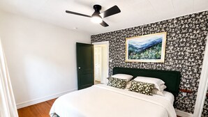 A bedroom with a bed, a ceiling fan, a door, and a wall with a floral pattern. - Couples King Bed Cottage with Fire Pit & Swing, Near Asheville & Biltmore in WNC (Leicester)