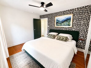 A bedroom with a bed, a ceiling fan, a door, and a wall with a floral pattern.
