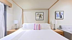 Une chambre d’hôtel avec un grand lit, deux tables de chevet, une chaise et des œuvres d’art accrochées aux murs.