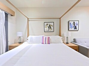Ein Hotelzimmer mit einem großen Bett, zwei Nachttischen, einem Sessel und Kunstwerken an den Wänden.