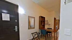 Une pièce avec une porte en bois sombre, une petite table avec des chaises, une bibliothèque en bois et un miroir fixé au mur.