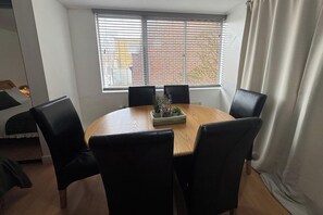 A round table with six chairs, a window with blinds, and a curtain. - 4 Bedroom Apartment Sleeps 14 With Balcony (London)