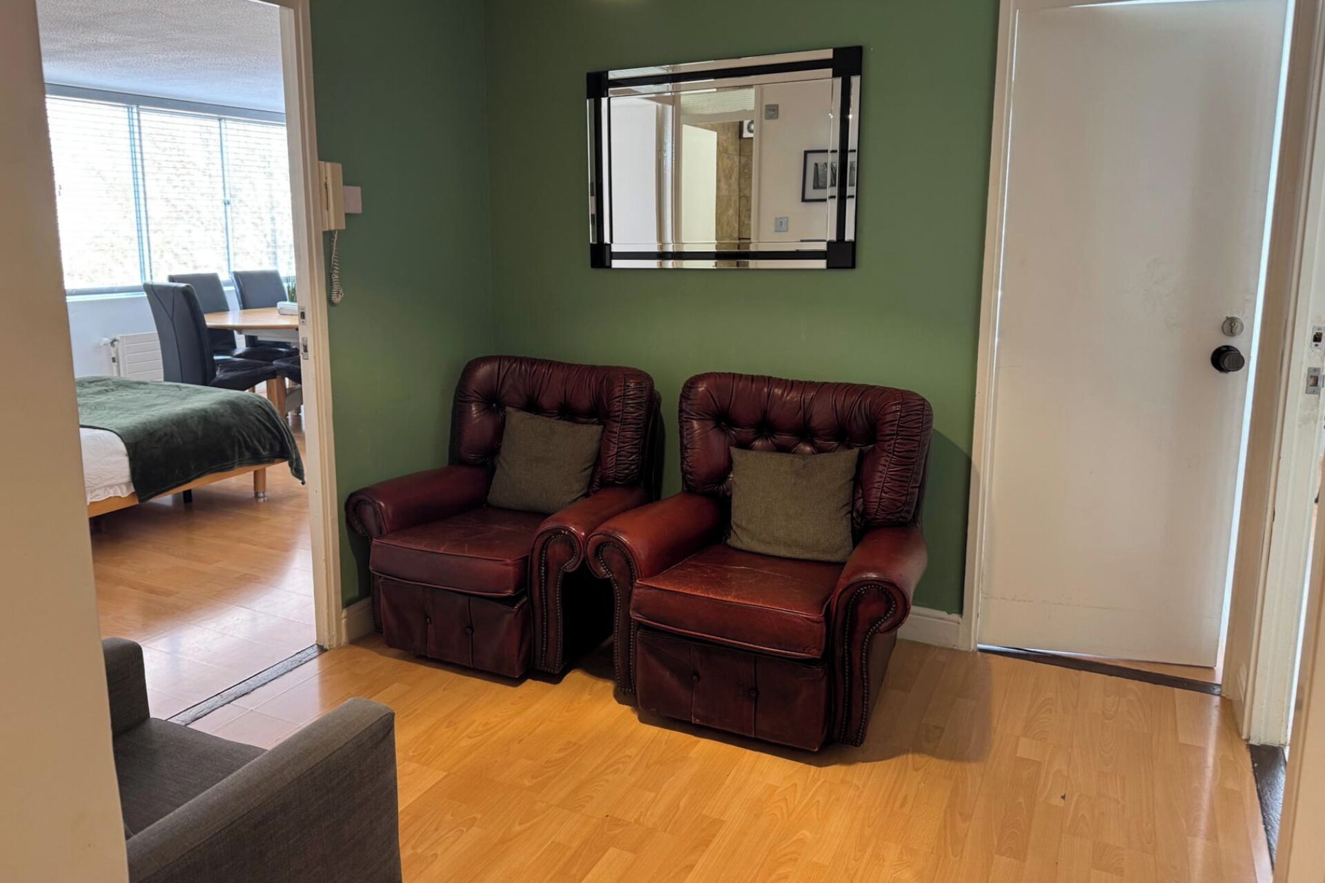Een kamer met twee leren fauteuils, een spiegel en een deur.