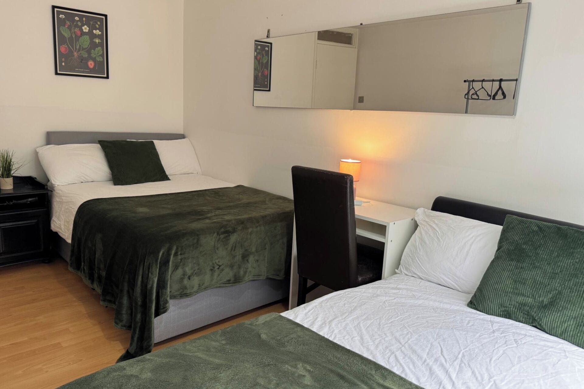 A room with two beds, a desk, a chair, a lamp, and a mirror.