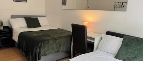 A room with two beds, a desk, a chair, a lamp, and a mirror.