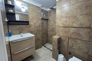 A bathroom with a sink, mirror, shelves with toiletries, and a shower area. - 4 Bedroom Apartment Sleeps 14 With Balcony (London)