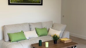 Un salon avec un canapé, des coussins, une table avec des bougies, une plante et un tableau encadré.