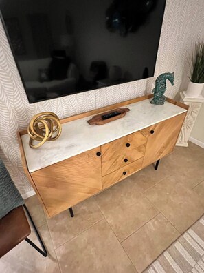 Un meuble TV en bois avec un plateau en marbre, une télécommande et un objet décoratif.