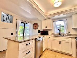 A modern kitchen with white cabinets, a granite countertop, a microwave, and a clock on the wall. - Coastal Escape Near Sanibel, Pool, Lanai & Beach Adventures - Tropical Tides Townhome - Roelens (Fort Myers)