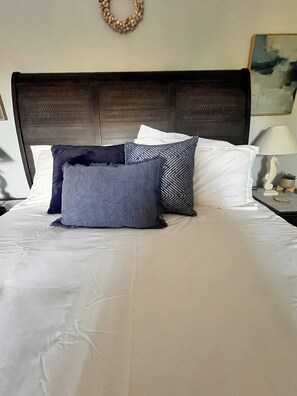 Un lit bien fait, avec une tête de lit sombre, des oreillers blancs et un coussin décoratif bleu.
