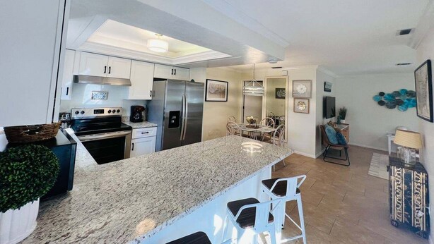 Een moderne keuken met witte kasten, een granieten aanrechtblad, roestvrijstalen apparatuur, en een eethoek met een tafel en stoelen.