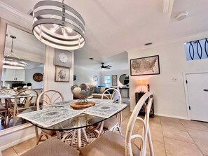 A dining area with a round glass table, wicker chairs, and a hanging light fixture. - Coastal Escape Near Sanibel, Pool, Lanai & Beach Adventures - Tropical Tides Townhome - Roelens (Fort Myers)