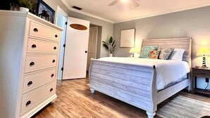 Een slaapkamer met een bed, een dressoir, een plafondventilator en een deur naar een andere kamer.