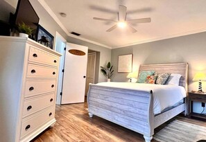 A bedroom with a bed, dresser, ceiling fan, and a door leading to another room. - Coastal Escape Near Sanibel, Pool, Lanai & Beach Adventures - Tropical Tides Townhome - Roelens (Fort Myers)
