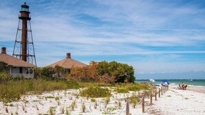Een strand met een vuurtoren, strandhutten en een zandstrand met mensen.