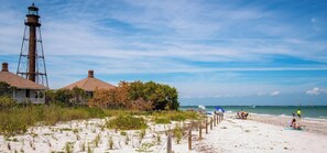 A beach with a lighthouse, beach huts, and a sandy shoreline with people. - Coastal Escape Near Sanibel, Pool, Lanai & Beach Adventures - Tropical Tides Townhome - Roelens (Fort Myers)