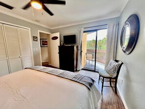 A bedroom with a bed, a ceiling fan, a TV, a wardrobe, a chair, and a balcony with a view. - Coastal Escape Near Sanibel, Pool, Lanai & Beach Adventures - Tropical Tides Townhome - Roelens (Fort Myers)