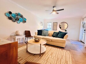 Un salon avec un canapé beige, une table basse ronde, un fauteuil marron et un ventilateur de plafond.