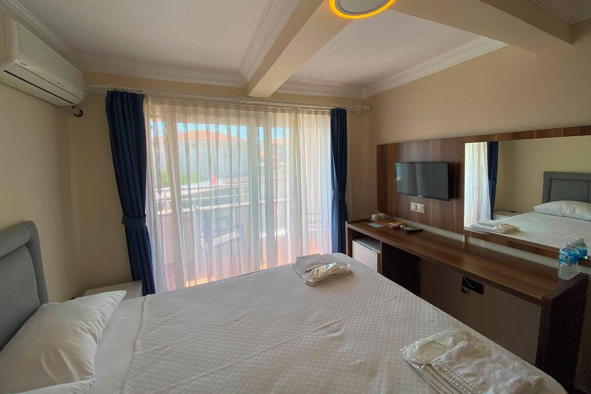 A hotel room with a bed, a desk, a television, and a window with curtains.