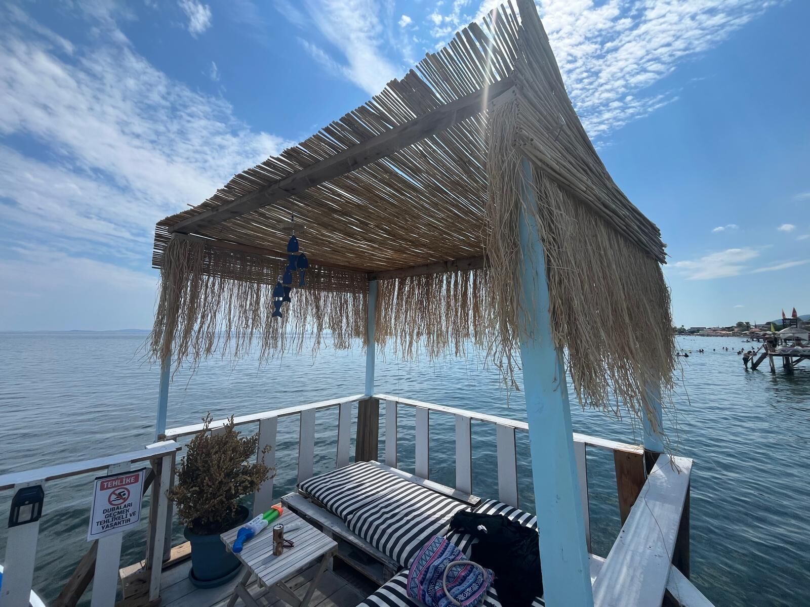 A wooden deck with a thatched roof, a bench, and a sign indicating a no smoking area.