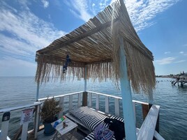 Una terraza de madera con techo de paja, un banco y un letrero que indica zona prohibido fumar.