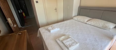 Una habitación de hotel con cama, armario, escritorio y puerta que da a un pasillo.
