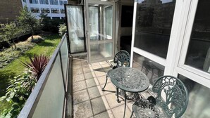 Un balcone con una porta in vetro, due sedie in metallo e un tavolino.