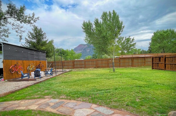 A fenced outdoor area with a wooden building, a stone pathway, and a grassy lawn.