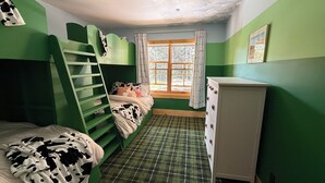 Une chambre avec un lit superposé, une commode, une fenêtre avec des rideaux et un tapis à carreaux.
