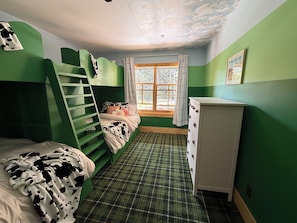 Una habitación con una cama litera, un aparador, una ventana con cortinas y una alfombra escocesa.